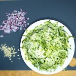 Die grob geraspelte Zucchini, die in Würfel geschnittene Zwiebel und der gehackte Knoblauch.